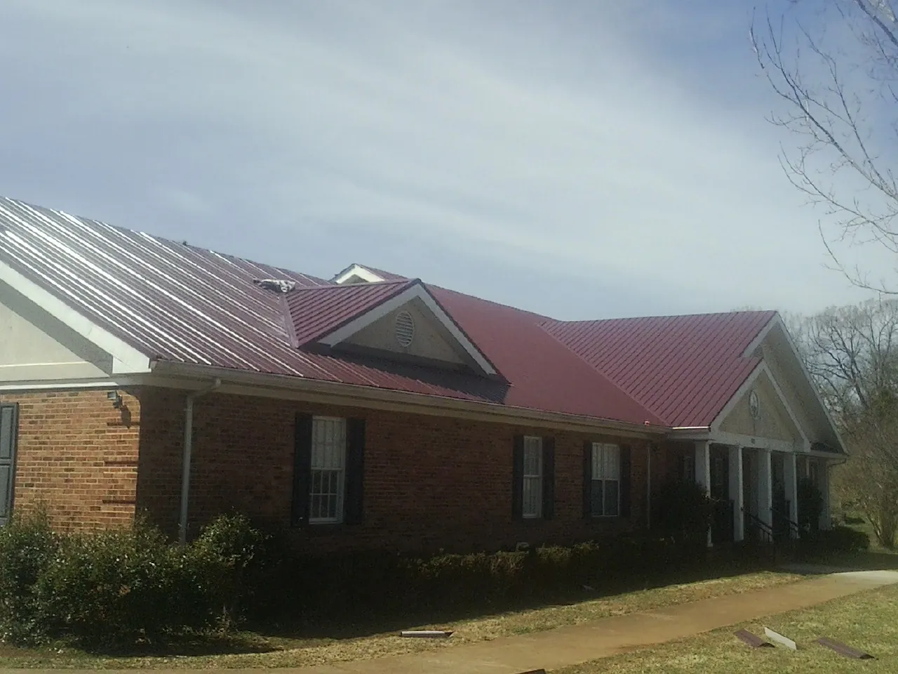 Red metal roof with gabled entries on a long brick building, from a Hail Damage Roof Repair job in Mc Clellandtown