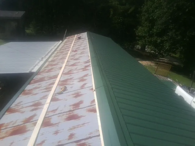 Old rusted panels beside newly installed green metal roofing — Wind Damage Roof Repair by Roofing Brothers in Mc Clellandtown