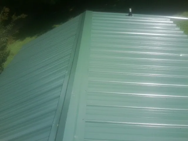 New green metal panels meeting at the ridge of a roof — Flat Roof Repair work by our crew in Mc Clellandtown