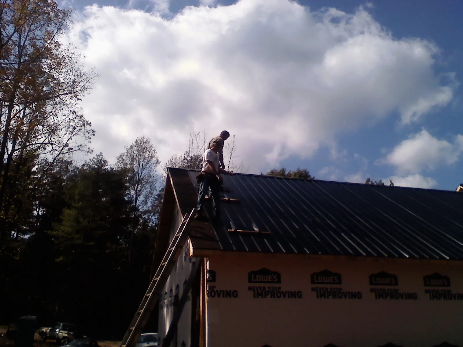 Roofer fastening dark metal panels high against a cloudy sky, from a Roof Inspection job in Mc Clellandtown