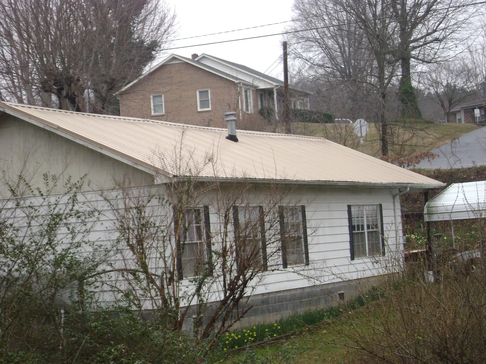 Tan metal roof on a white sided house set into a hillside — Commercial Roofing by Roofing Brothers in Mc Clellandtown