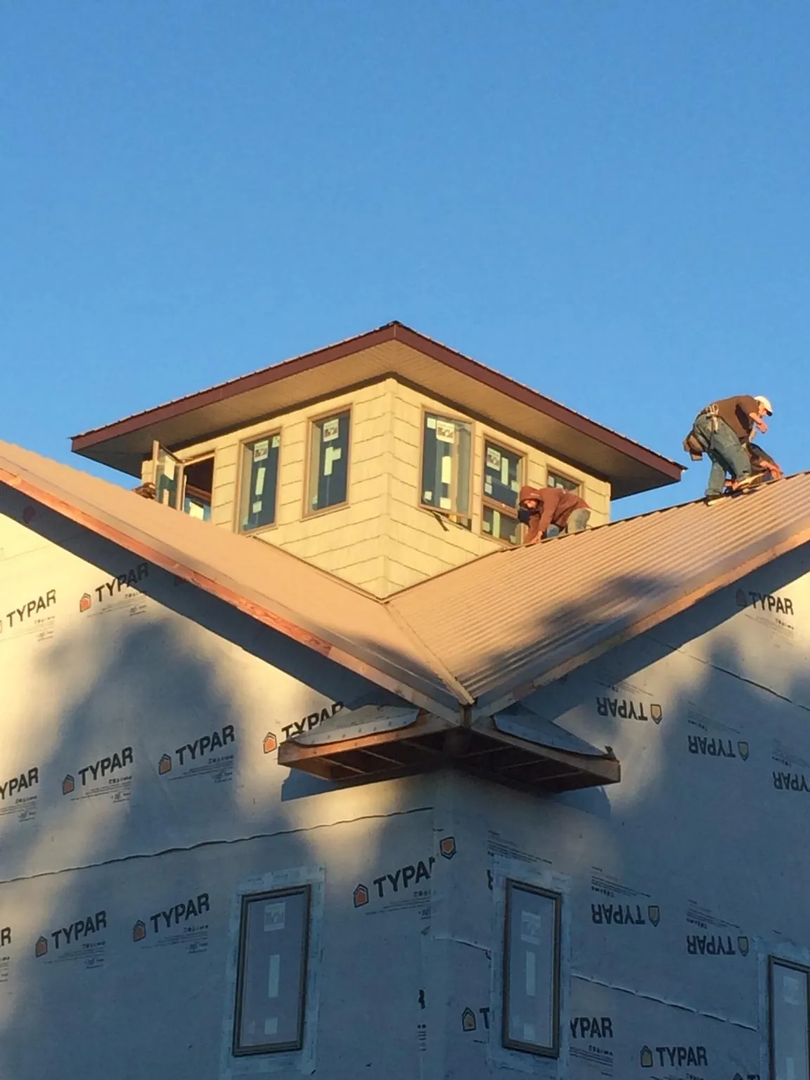 Roofers working around a rooftop cupola on a new metal roof at sunset — Roof Waterproofing in Mc Clellandtown by Roofing Brothers